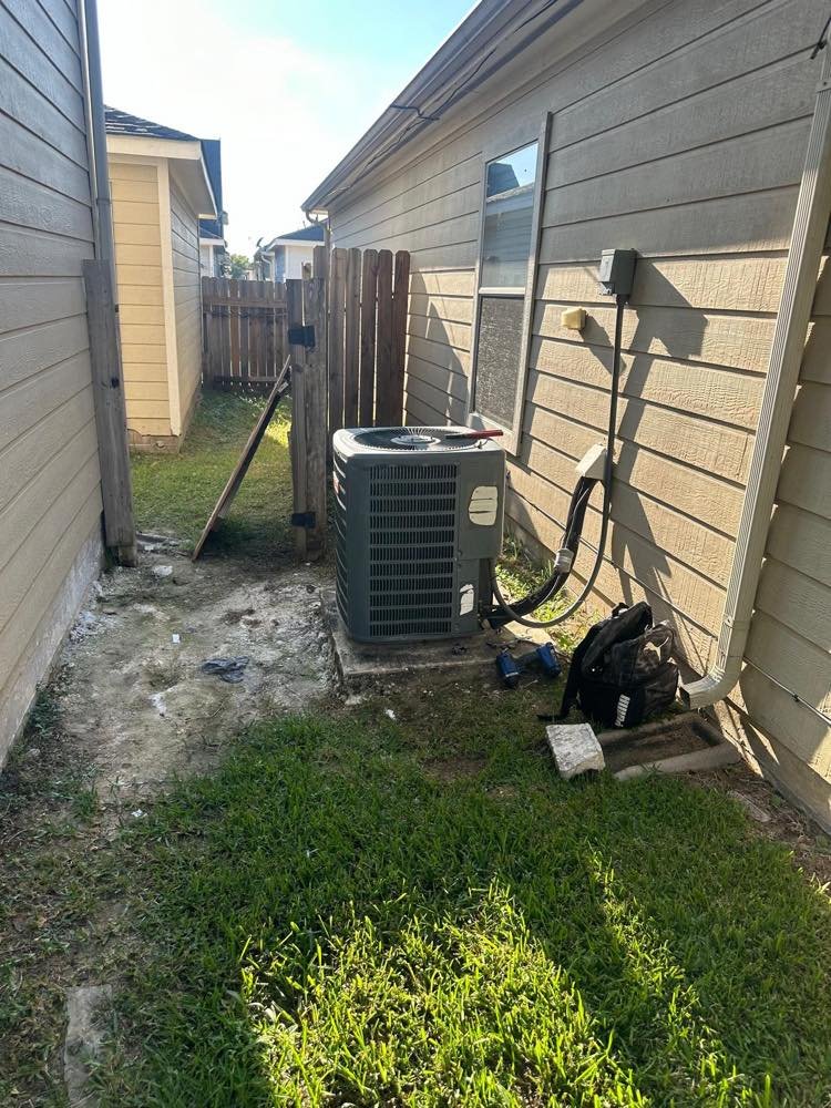 Condensador de aire acondicionado en el pasillo lateral de una vivienda de Houston, con una mochila de herramientas en el suelo