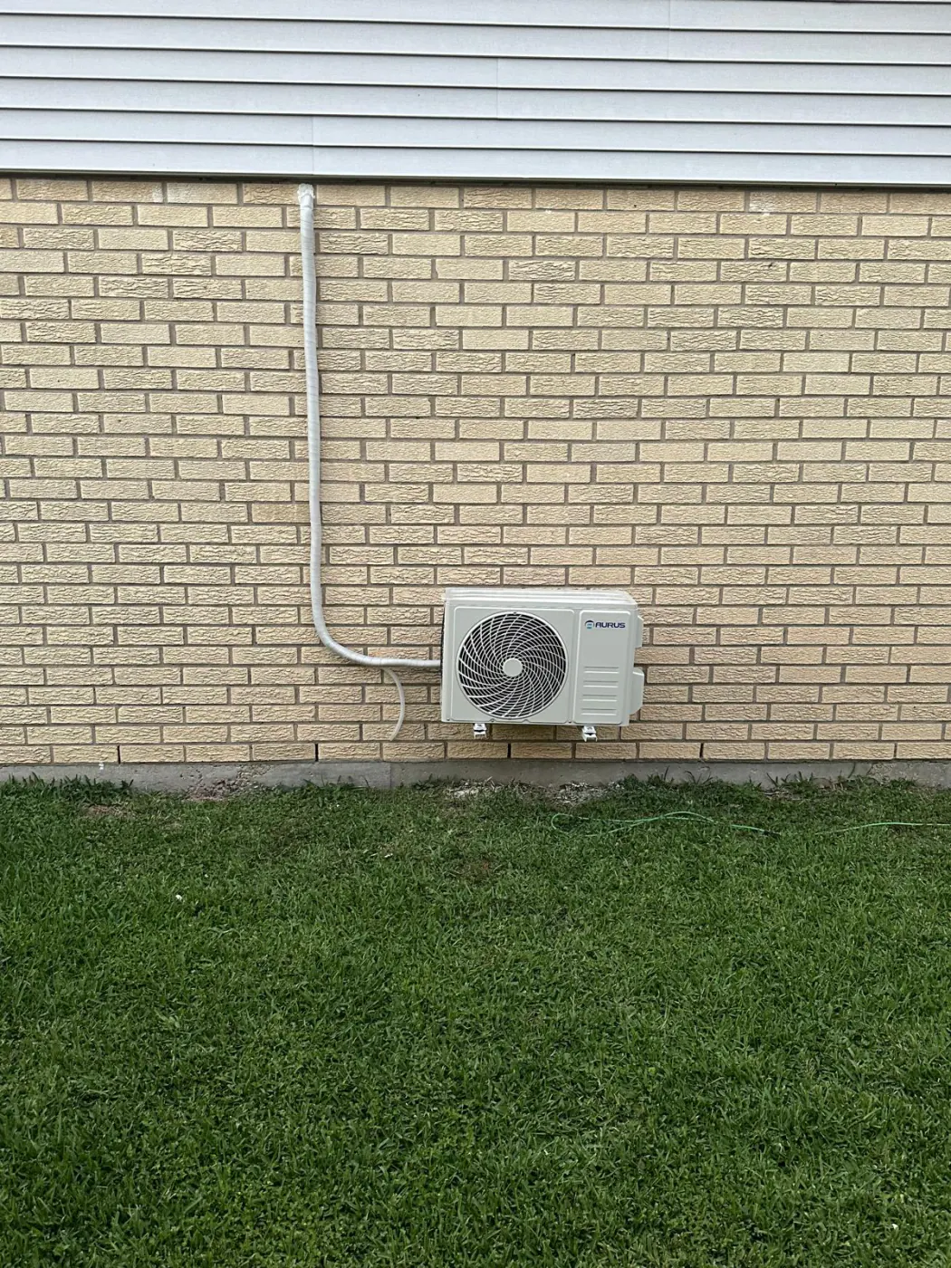 A mini-split outdoor unit mounted on a brick wall, with the line set run neatly to the equipment